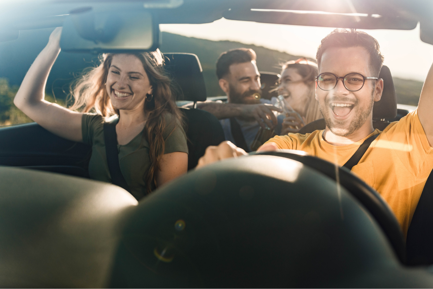 A group of four friends drive, smiling and laughing, with a sunset behind them