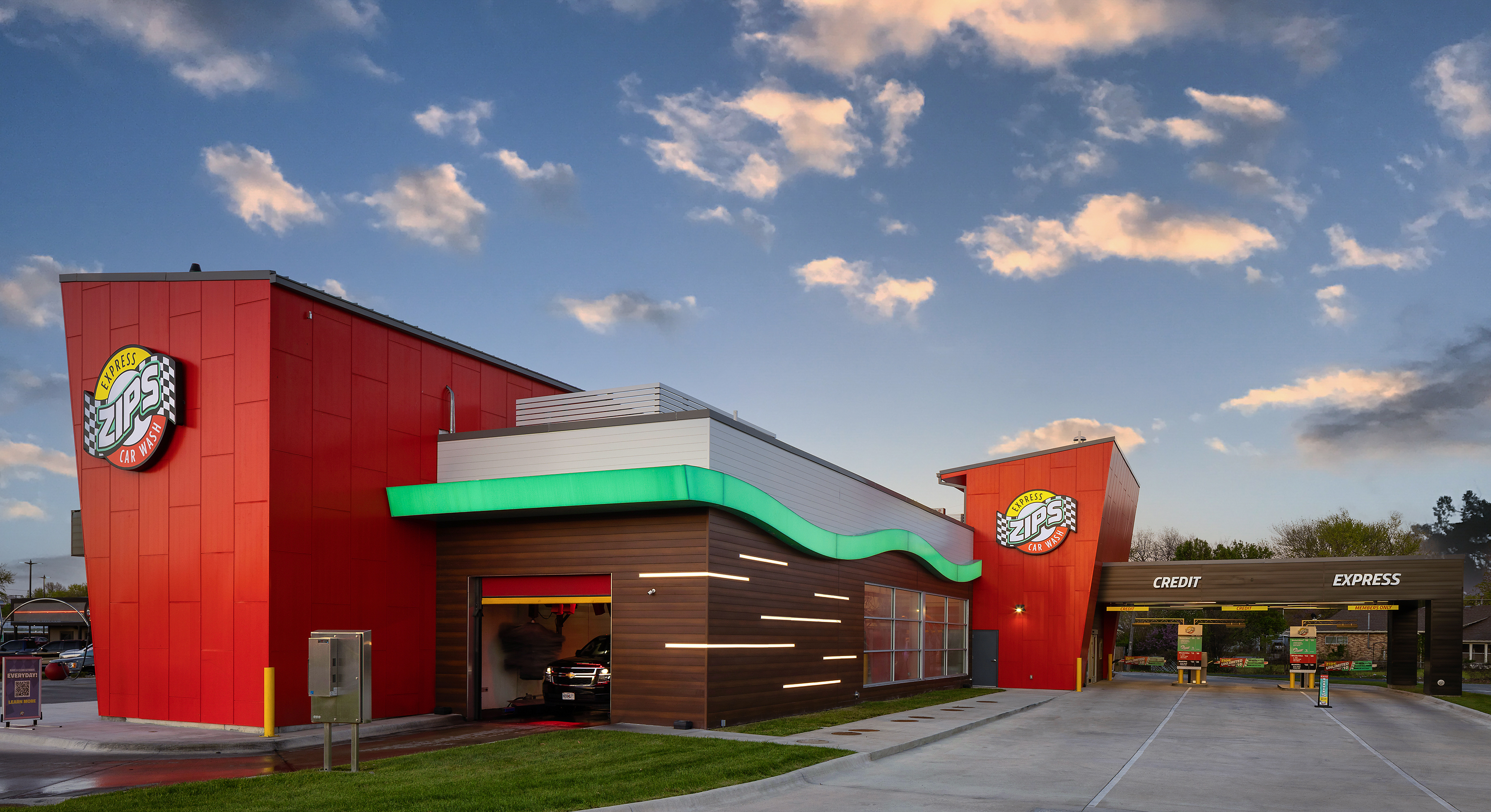Car wash exterior of a full ZIPS Car Wash including lane entrance and tunnel exit against a blue sky with clouds