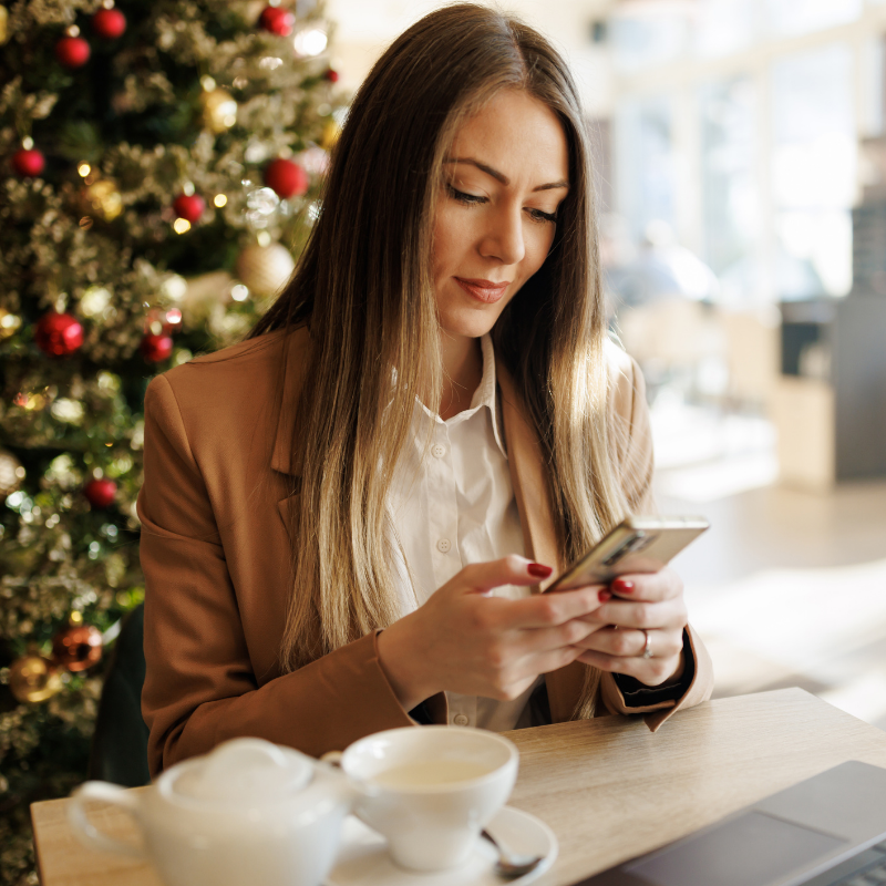Woman smiling at her phone at a cafe decorated for the holidays